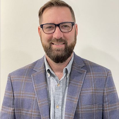 A bearded man wearing glasses and a plaid blazer specializing in web design and brand development.