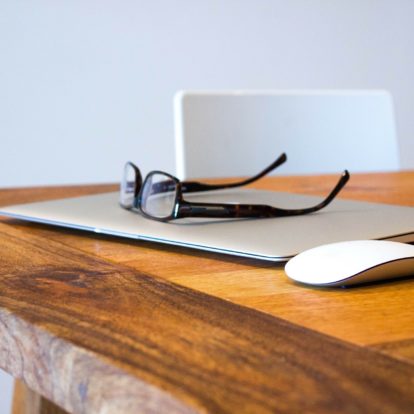 A sleek laptop rests on a polished wooden desk, adorned with stylish glasses and a functional mouse. This setup is perfect for individuals involved in branding and design, especially web design.